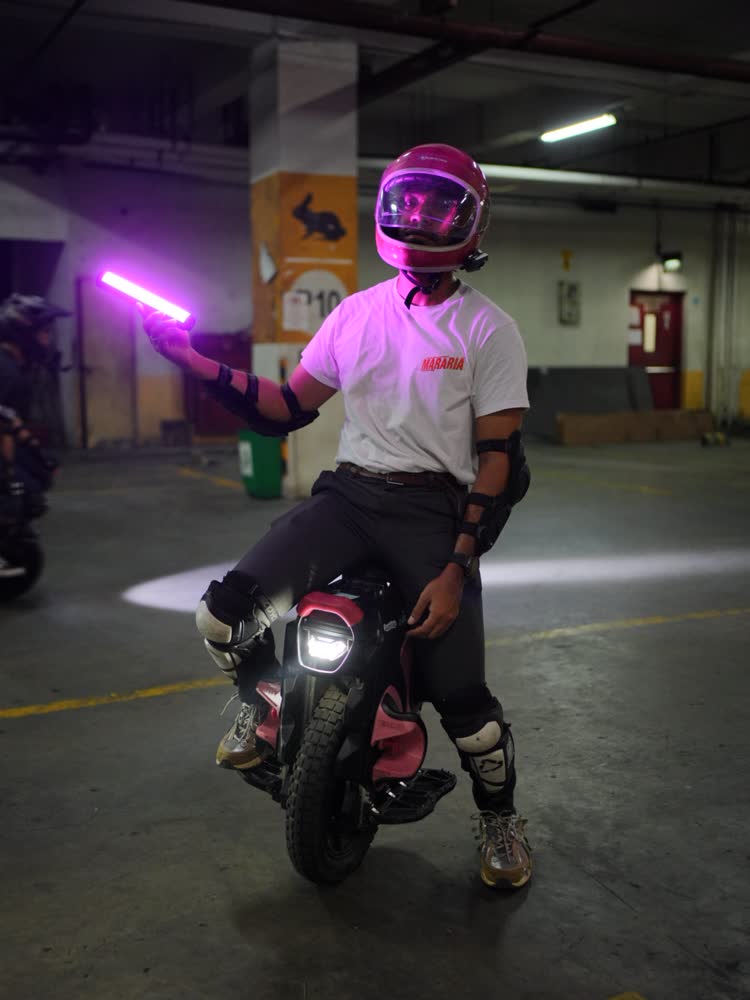 Rider in a pink helmet holding a purple light tube in a parking garage
