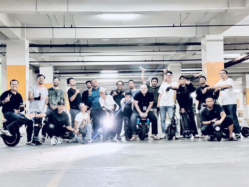 Group of riders posed together with a headlight flaring into the lens