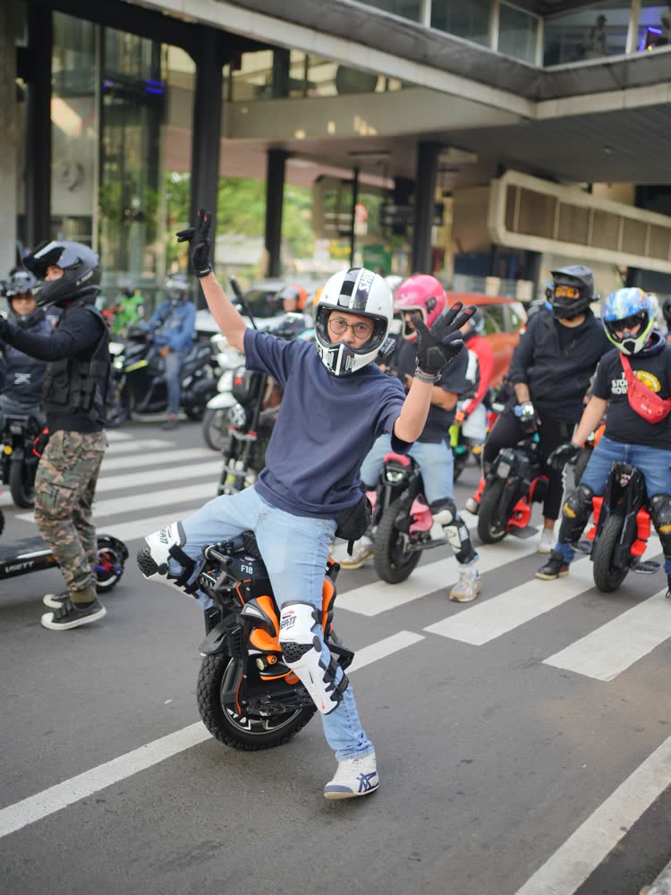 Rider waving while crossing a Jakarta street with towers behind